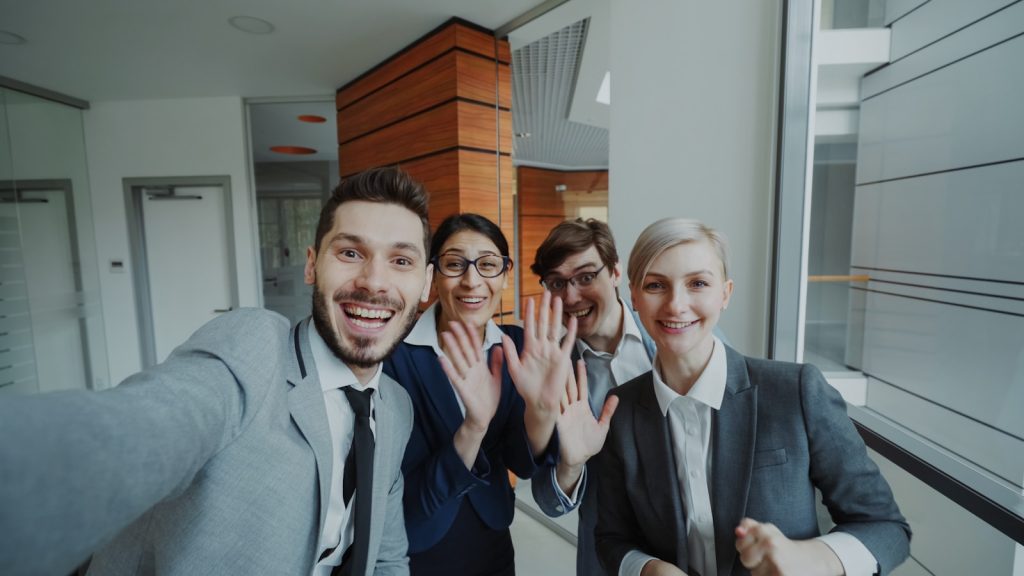 Four business people smiling and waving at camera.
